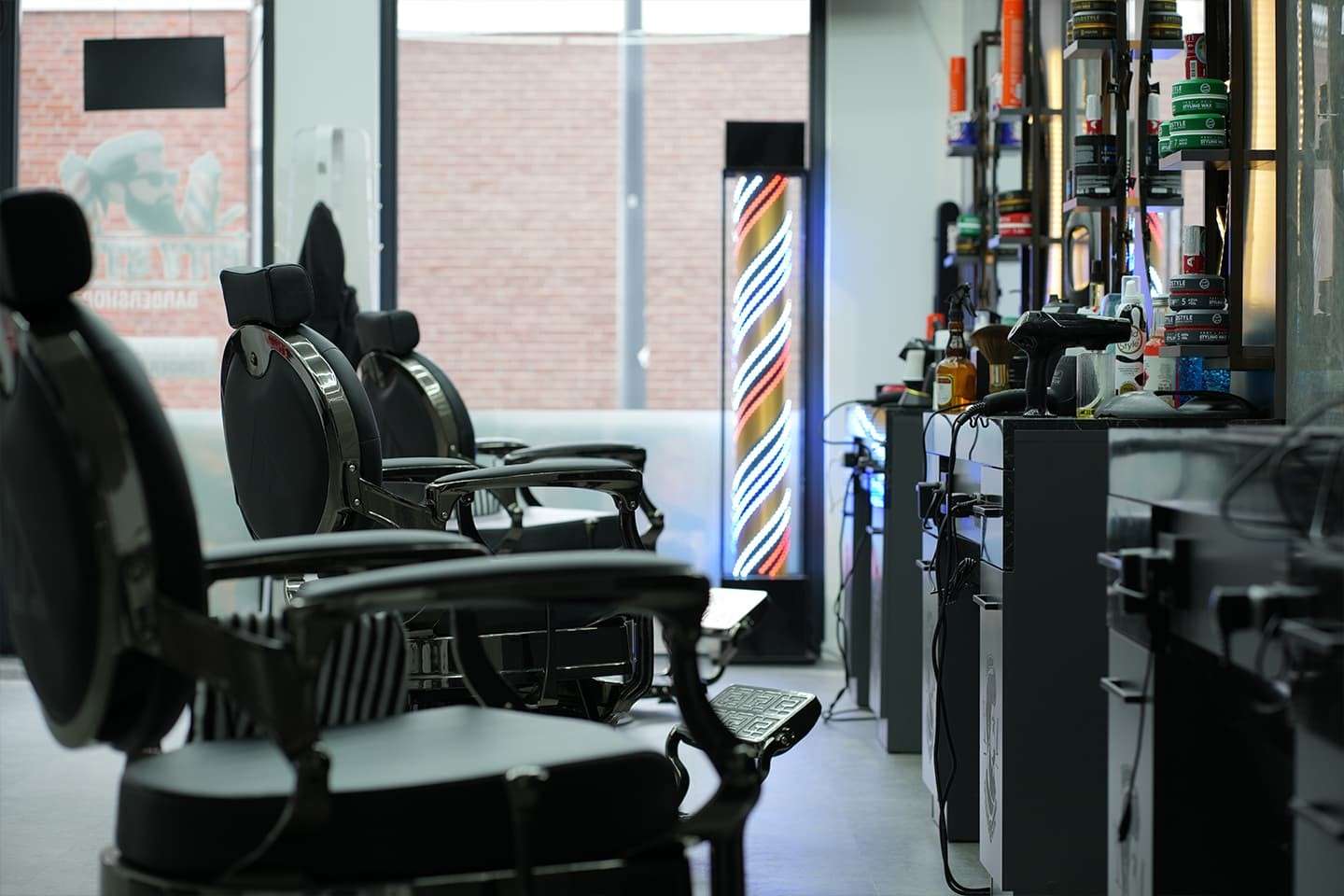 Barberstoelen van opzij met een verlichte barberpaal bij City Style Barbershop